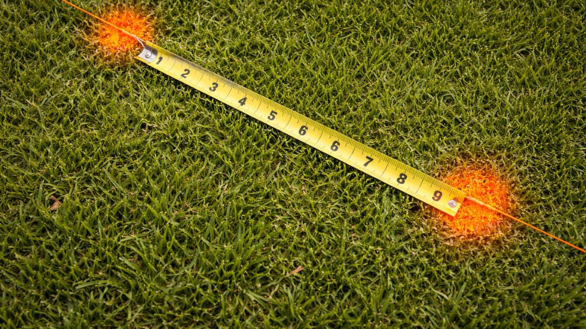Post hole locations marked with orange spray paint dots along fence string line, tape measure showing spacing