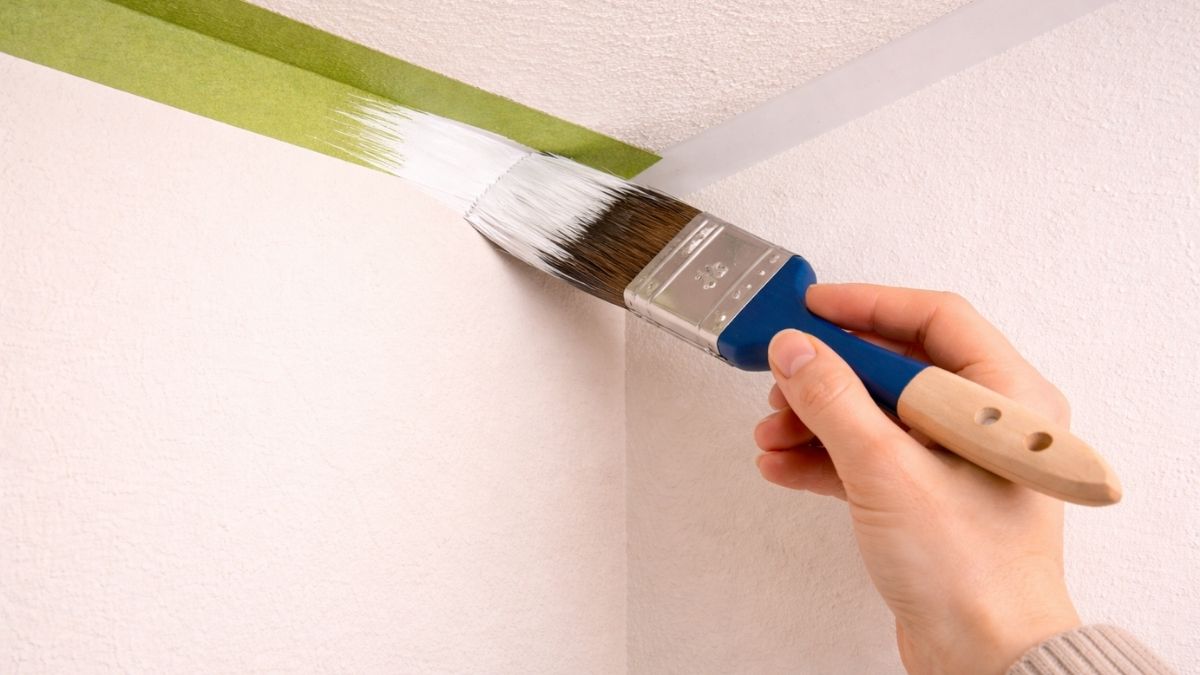Angled sash brush cutting in paint along ceiling line at wall corner